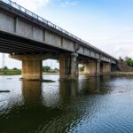A large concrete bridge spanning a calm river under a clear sky, showcasing modern infrastructure.